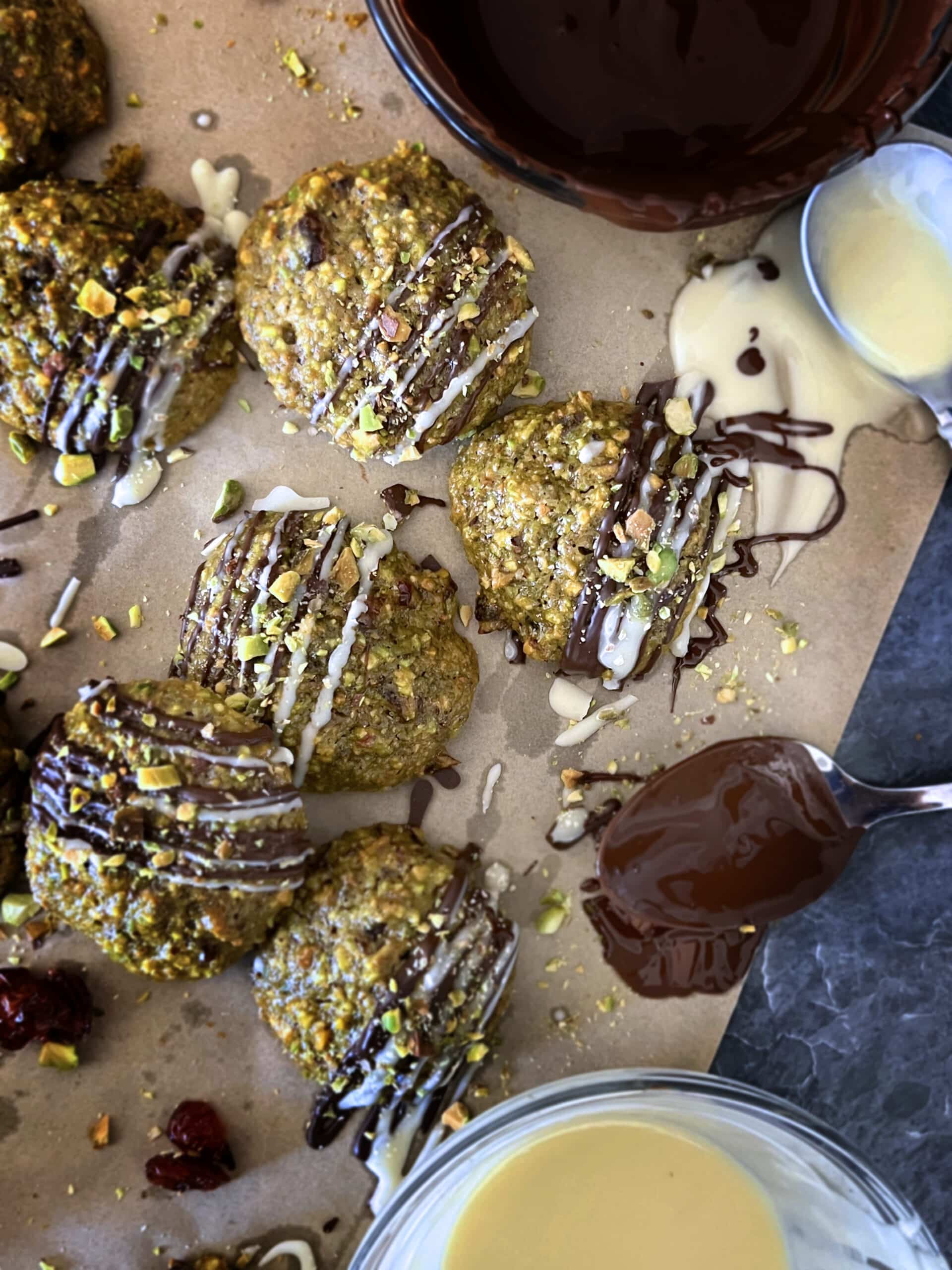 Aerial view of Pistachio Cranberry Cookies arranged on parchment with melted dark and white chocolat